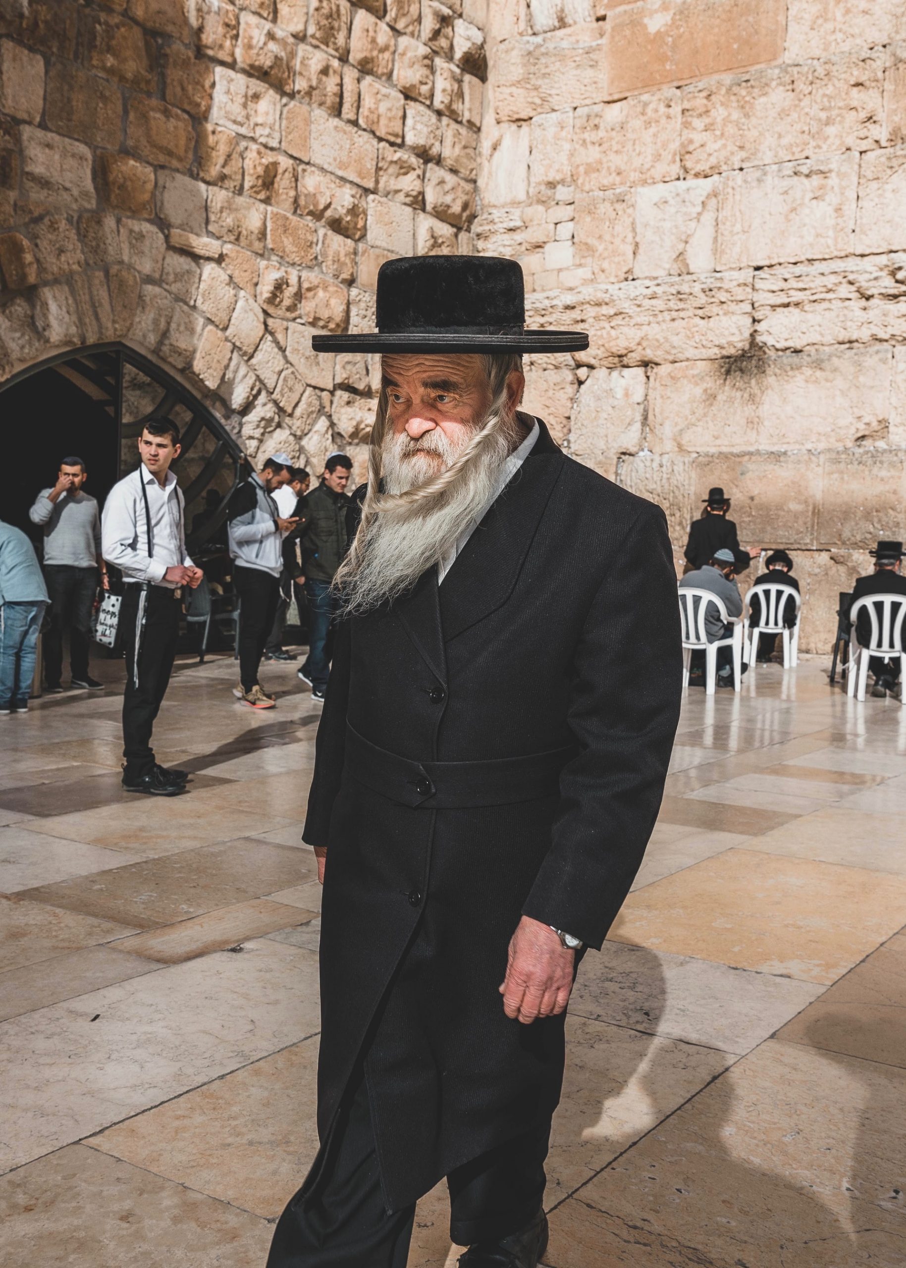 Elderly man in black traditional attire walking near the Western Wall